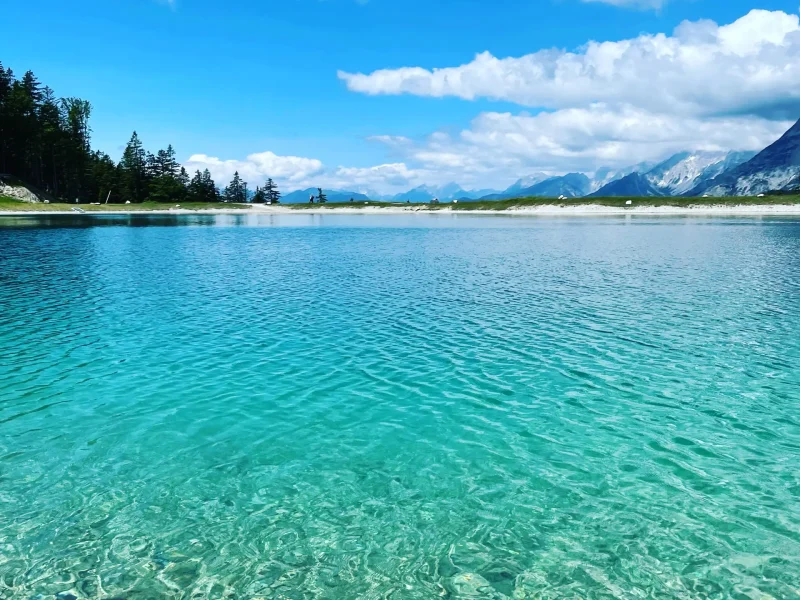 Kristallklarer Bergsee mit türkisem Wasser in Tirol, umgeben von Bergen und blauem Himmel